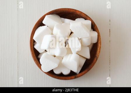 Brückenförmiger Rübenzucker in Holzschüssel auf einem weißen Holztisch. Flach liegend, Blick von oben nach unten, keine Leute. Stockfoto