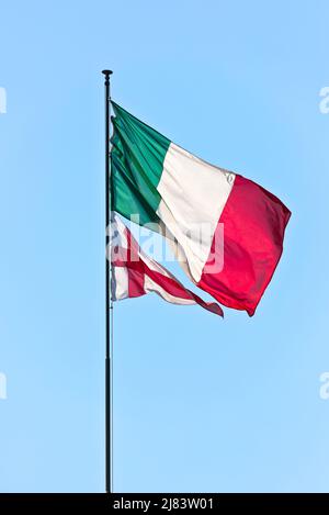 Nationalflagge Italiens und Flagge Genuas, Hauptstadt der italienischen Region Ligurien, winken im Wind vor klarem blauen Himmel Hintergrund Stockfoto