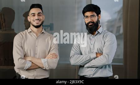 Zwei männliche Freunde multirassische verschiedene Kollegen Geschäftspartner hispanic Mann arabian bärtig Kerl im Büro stehend mit gekreuzten Armen nickend posieren Stockfoto