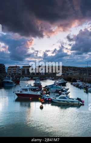 West Bay, Dorset, Großbritannien. 12. Mai 2022. Wetter in Großbritannien. Dunkle, bedrohliche Wolken über dem Hafen während des Sonnenuntergangs im Badeort West Bay in Dorset. Bildnachweis: Graham Hunt/Alamy Live News Stockfoto