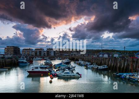 West Bay, Dorset, Großbritannien. 12. Mai 2022. Wetter in Großbritannien. Dunkle, bedrohliche Wolken über dem Hafen während des Sonnenuntergangs im Badeort West Bay in Dorset. Bildnachweis: Graham Hunt/Alamy Live News Stockfoto