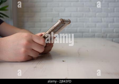 Hände eines Teenagers, der sich auf einen weißen Holztisch lehnte und das Mobiltelefon hielt Stockfoto