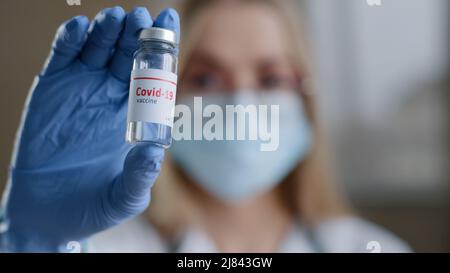 Nahaufnahme Fachchemikerin Biochemikerin Ärztin Krankenschwester Wissenschaftlerin in einer medizinischen Maskenbrille und Latexhandschuhen, die auf die Kamera mit der Flasche blicken Stockfoto