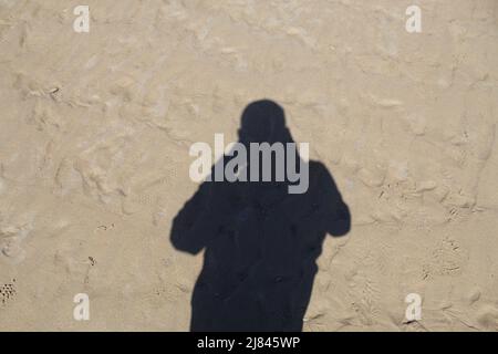 Der Schatten eines Fotografen im Sand am Crosby Beach in Liverpool, Großbritannien. Das Foto wurde an einem heißen Sommernachmittag aufgenommen, als die Flut war Stockfoto