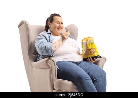 Mollige Frau, die in einem Sessel sitzt und Tortilla-Chips auf weißem Hintergrund isst Stockfoto