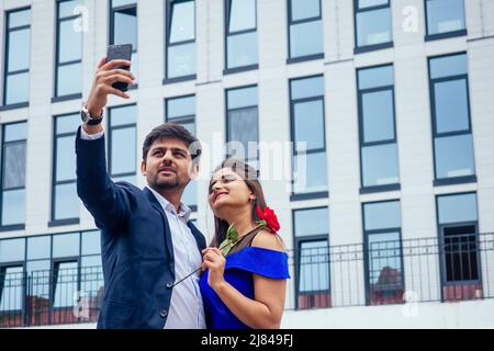 Glücklicher asiatischer Mann in stilvollem schwarzen Anzug macht Selfie-Foto mit seiner schönen Frau nach Vorschlag und geben Goldring auf dem Hintergrund der Stockfoto