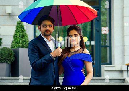 indische Frau in langen Abend blau Kleid Spinnen romantische Zeit zusammen mit Liebhaber schöner Freund unter bunten Regenbogen Regenschirm europa Stockfoto