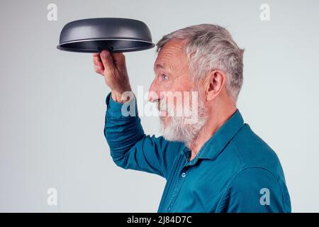 Mann alt hält Braten Metall Antihaftpfanne im Studio weißen Hintergrund Stockfoto