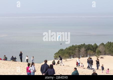 Foto von Touristen auf der Dune du Pilat vor einem Gleitschirm in der Bucht von Arcachon, Frankreich. Die Düne von Pilat, auch Grande Dune du Pilat genannt, ist die große Stockfoto