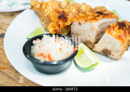 45-Grad-Foto eines Tellers mit gebratener Schweineschulter und würzigem Zwiebelsalat. Traditionell aus Lateinamerika Stockfoto