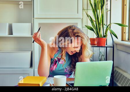 Junge Studentin mit Laptop und einer Tasse Kaffee, die zu Hause online lernt Stockfoto