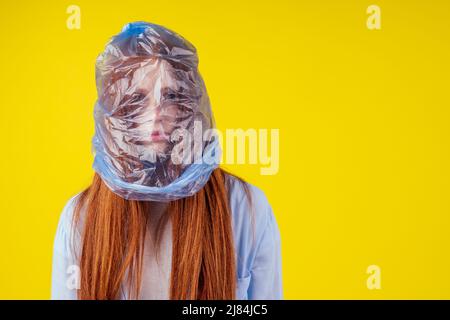 Rothaarige Ingwer europäische Frau Erstickungskopf in blauen Polyethylen-Paket in Studio gelben Hintergrund. Eco Verschmutzung Cellophan Film Konzept Stockfoto