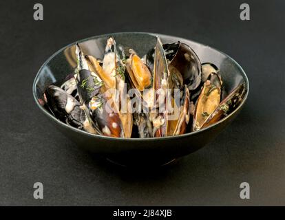 Muscheln in cremiger Soße auf einem schwarzen Teller auf schwarzem Hintergrund Stockfoto