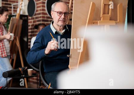 Porträt eines älteren Mannes Studenten sitzen in der Kunstklasse vor auf Leinwand Zeichnung Vase Modell mit Bleistift. Vielfältiges Team, das an der Skizzierungstechnik arbeitet und künstlerische Fähigkeiten entwickelt. Kreatives Konzept Stockfoto