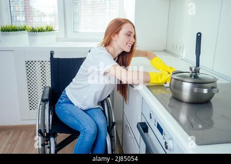 Junge rothaarige Ingwer behinderte Frau im Rollstuhl tragen gelbe Ribon Handschuhe und Reinigung Wohnung Stockfoto