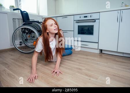 Rothaarige Ingwerfrau, die im Küchenzimmer herunterfiel und um Hilfe kriecht Stockfoto