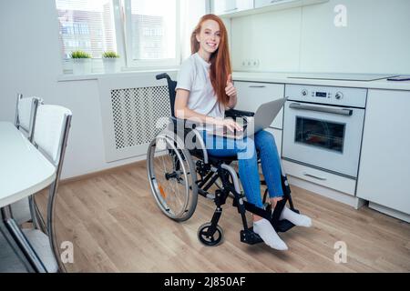 Rothaarige Ingwerfrau im Rollstuhl in der Küche Stockfoto