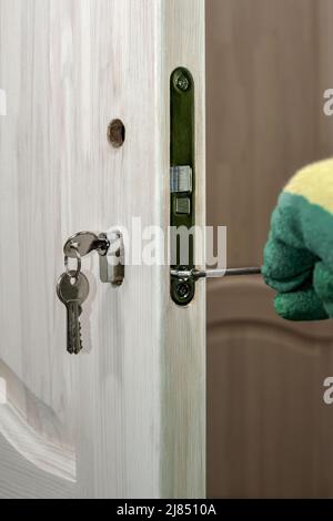 Installation eines Schlosses an einer Holztür. Einbau und Austausch des Zylinders durch Schlüssel für das Türschloss. Stockfoto