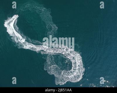 Luftaufnahme von oben nach unten von Wasserschaumspuren mit schönem tiefblauen Schatten des Ozeans. Schöne weiße Spur auf der ruhigen Meeresoberfläche hinter einem kleinen mächtigen Stockfoto