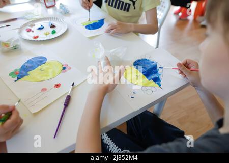 Bukarest, Rumänien - 9. Mai 2022: Details zur geringen Schärfentiefe (selektiver Fokus) mit ukrainischen Flüchtlingskindern, die eine herzförmige ukrainische Flagge zeichnen Stockfoto