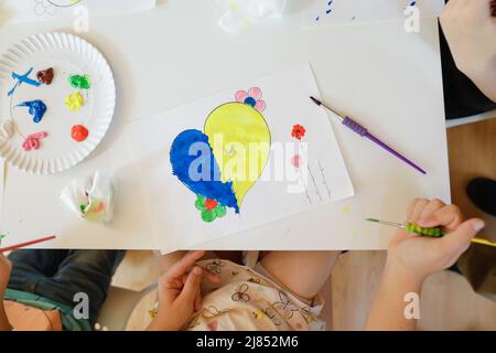 Bukarest, Rumänien - 9. Mai 2022: Details zur geringen Schärfentiefe (selektiver Fokus) mit ukrainischen Flüchtlingskindern, die eine herzförmige ukrainische Flagge zeichnen Stockfoto