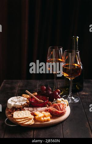 Wurst und Käse, geschnitten mit Obst, Keksen und Sauce, mit zwei Gläsern weißem Portwein und einer Flasche. Aufschnitt und Käseplatte Stockfoto