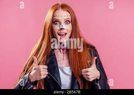 Rothaarige Ingwer Biker Frau trägt schwarze Lederjacke mit Blut Make-up Chirurgie Nase und Hals Bruch für halloween-Party, Studio rosa Hintergrund Stockfoto