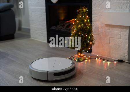 Roboter-Staubsauger, der den Raum in der Nähe eines Weihnachtsbaums reinigt Stockfoto