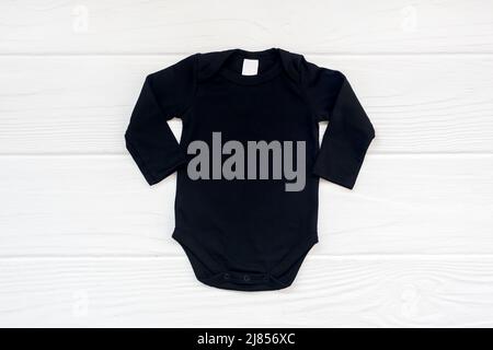 Schlichtes schwarzes Baby Body Langarm Flatlay Mockup auf weißem Holz Hintergrund. Stockfoto