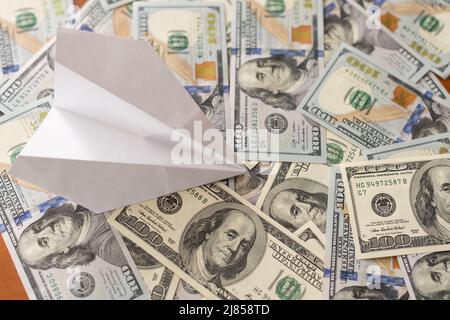 origami-Flugzeug landet auf einem Stapel von Banknoten aus dem US-Dollar. Stockfoto