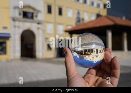 Hand hält Glaskugel vor dem alten Stadttor und Marktplatz in Cres (Kroatien) Stockfoto