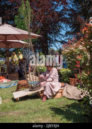 Beervelde, Belgien, 8. Mai 2022, Lady in einem Vintage-Gewand webt einen Korb auf einer Holzkiste Stockfoto