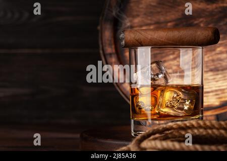 Glas mit Whiskey, Cognac oder goldenem Rum und Zigarre. Vor einem alten Holzfass mit Kopierraum Stockfoto