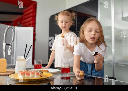 Zwei kleine Mädchen Geschwister haben Spaß und essen in der Küche zu Hause mit japanischer Nahrung. Stockfoto