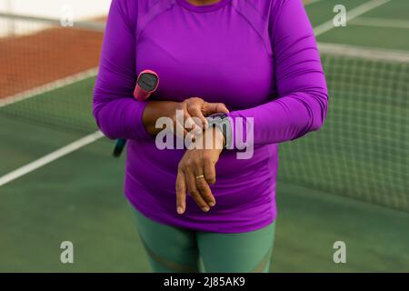 Mittelteil einer älteren Frau mit Schläger und Zeitkontrolle über die Armbanduhr auf dem Tennisplatz Stockfoto