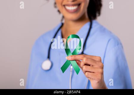 Mittelteil einer lächelnden afroamerikanischen Ärztin mit mittlerem Erwachsenen und grünem Bewusstseinsband Stockfoto