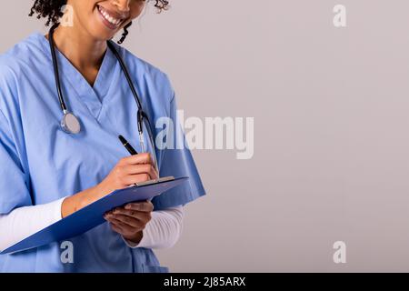 Mittelteil einer glücklichen afroamerikanischen Ärztin mit mittlerem Erwachsenen und Stethoskop-Schrift auf der Zwischenablage Stockfoto