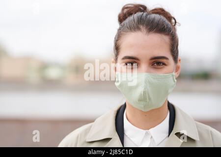 Portrait einer attraktiven jungen Geschäftsfrau in Stoffmaske, die während des Coronavirus mit Schutzthing nach draußen geht Stockfoto