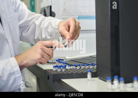 Wissenschaftler im Labormantel, der das Fläschchen mit der Probe in den Autosampler des HPLC-Systems eingibt. Stockfoto