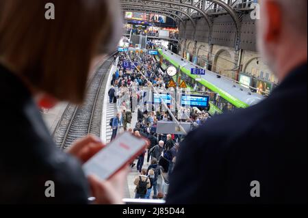 Hamburg, Deutschland. 13.. Mai 2022. Zahlreiche Reisende stehen auf einem Bahnsteig am Hamburger Hauptbahnhof, während eine Frau auf ihrem Handy nach einer Zugverbindung sucht. Aufgrund eines Kabelbrands in Hamburg ist der Fernverkehr stark gestört. Quelle: Jonas Walzberg/dpa/Alamy Live News Stockfoto