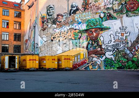 Geparkte Lastwagen des DHL International Courier neben einer mit Graffiti und Street Art bedeckten Wand in Kreuzberg, Berlin. Kurier-, Paket- und Express-Postdepot der Deutschen Post Stockfoto