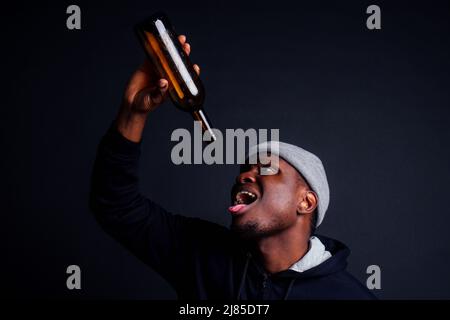 afroamerikanische gue trägt grauen Hut und Hoody hjlding Botle mit Wein in srudio schwarzen Hintergrund.Alkoholismus Obdachlosen bum Konzept Stockfoto