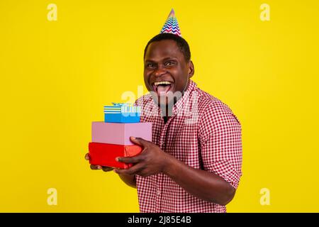 Glücklicher afroamerikanischer Mann, der Kisten mit Geburtstags-Geschenken auf gelbem Hintergrund hält Stockfoto