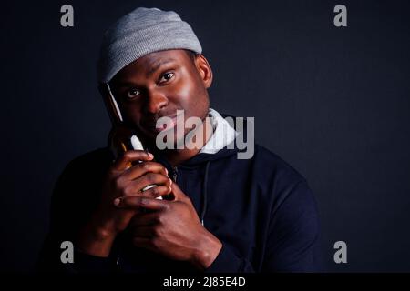 afroamerikanische gue trägt grauen Hut und Hoody hjlding Botle mit Wein in srudio schwarzen Hintergrund.Alkoholismus Obdachlosen bum Konzept Stockfoto