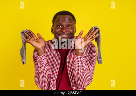 Unzufriedener afroamerikanischer Mann schließt die Nase, fühlt sich über Socken übel gerochen, trägt lässiges rotes T-Shirt auf Studio-gelbem Hintergrund Stockfoto