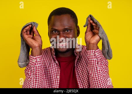 Unzufriedener afroamerikanischer Mann schließt die Nase, fühlt sich über Socken übel gerochen, trägt lässiges rotes T-Shirt auf Studio-gelbem Hintergrund Stockfoto