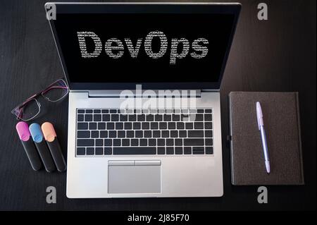 Draufsicht des Laptops mit Text DevOps. DevOps-Beschriftung auf dem Laptop-Bildschirm. DevOps kombiniert Softwareentwicklung und IT-Betrieb. Stockfoto