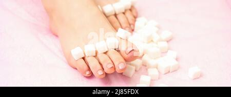 Das Konzept der Epilation, Wachsen. Zuckerwürfel liegen in einer Reihe auf weiblichen Füßen, Zehen über rosa Hintergrund Stockfoto