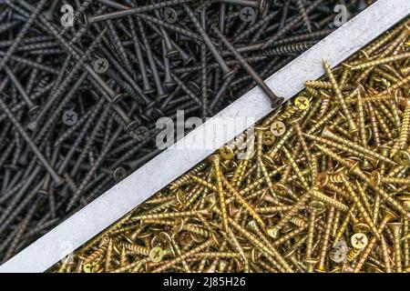 Viele selbstschneidende Schrauben aus Gold und schwarzem Metall. Stockfoto