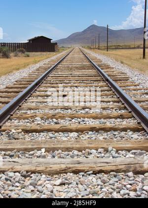 Bahn in der Wüste. Perspektivischer Blick mit blauem Himmel im Rücken. Landschaft in Utah USA. Eisenbahn mit Schroten Felsen und Eisenbahnstrümmer. Stockfoto